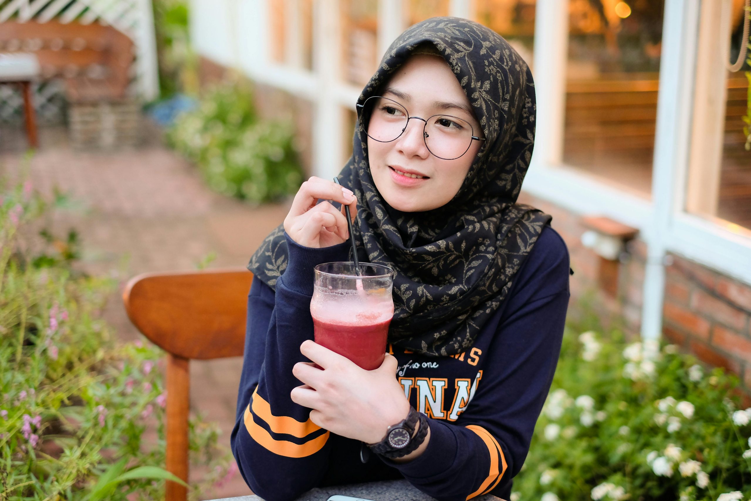 A woman in a hijab enjoys a refreshing drink while seated outdoors, depicting a moment of leisure.
